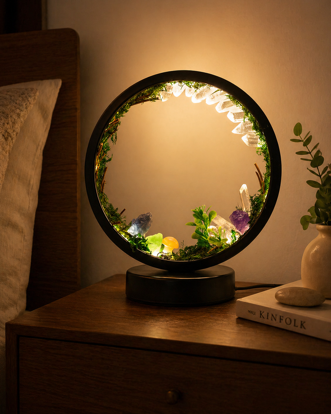 A round forest-style night light glowing on a wooden nightstand.